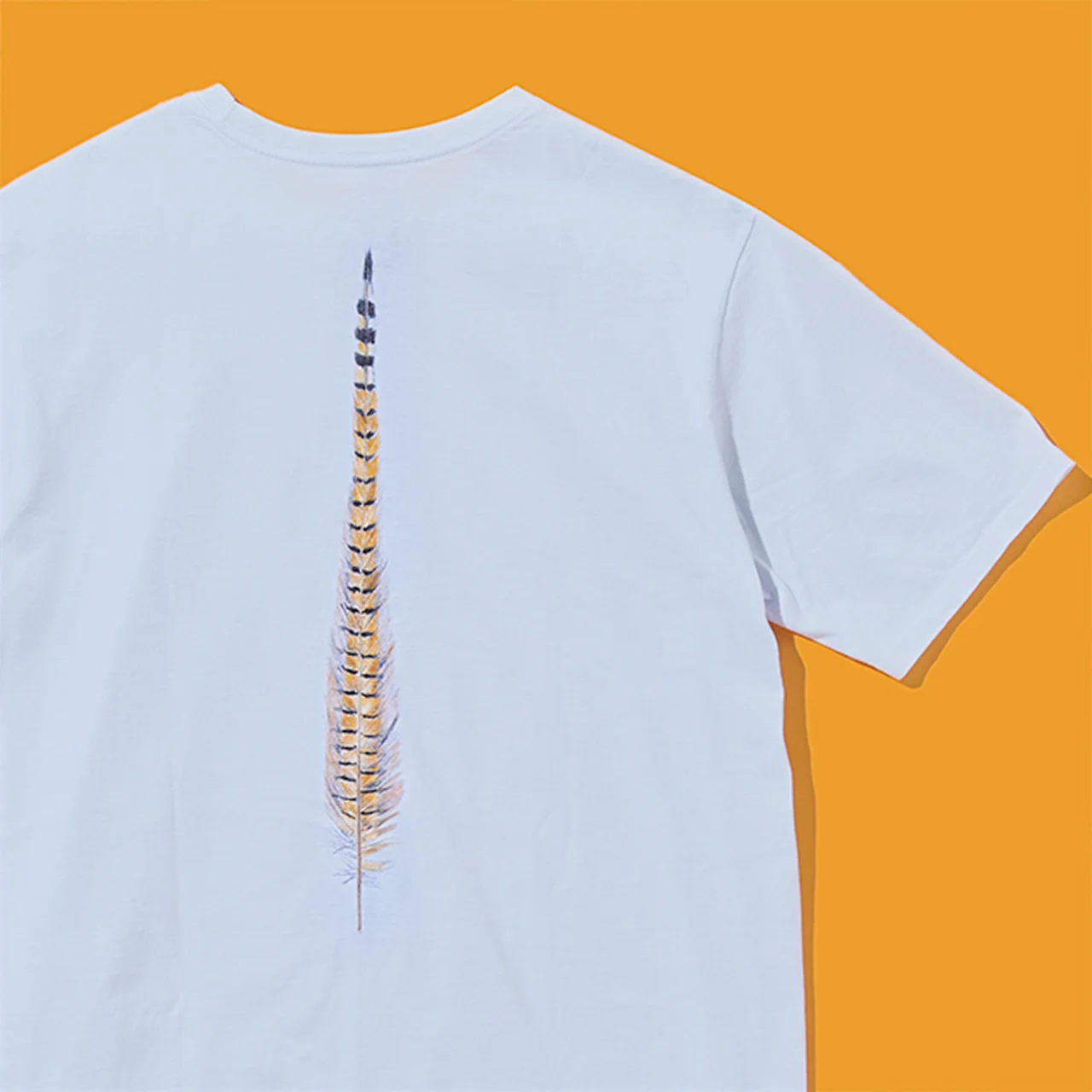 Tシャツのバックに、フライフィッシング用の毛バリとして使う『フェザントテイル（キジの尾羽）』が描かれている